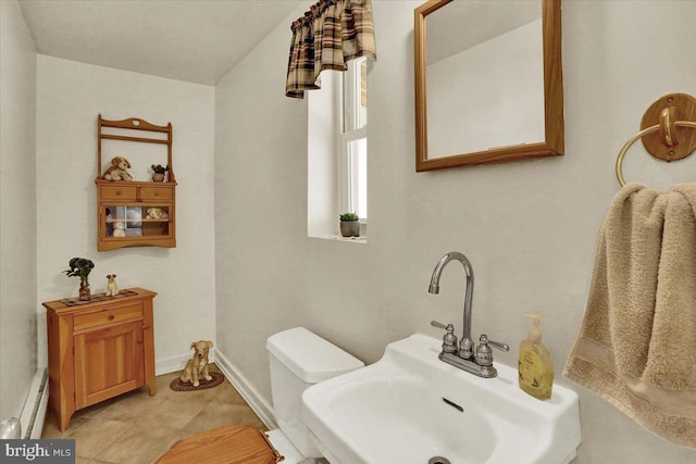 half bathroom featuring toilet, baseboards, baseboard heating, and a sink