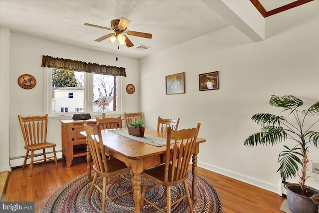 dining area featuring light wood-style flooring, a textured ceiling, a baseboard heating unit, and ceiling fan