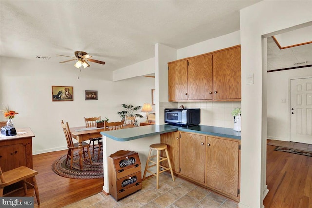 kitchen with visible vents, a peninsula, ceiling fan, light wood-style floors, and backsplash