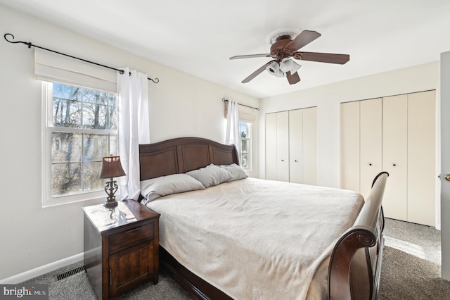 carpeted bedroom featuring baseboards, multiple closets, visible vents, and ceiling fan