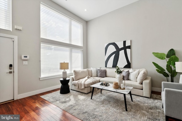 living area with baseboards, a towering ceiling, and hardwood / wood-style floors