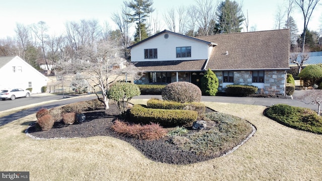 traditional-style house featuring a front lawn, stone siding, and a shingled roof