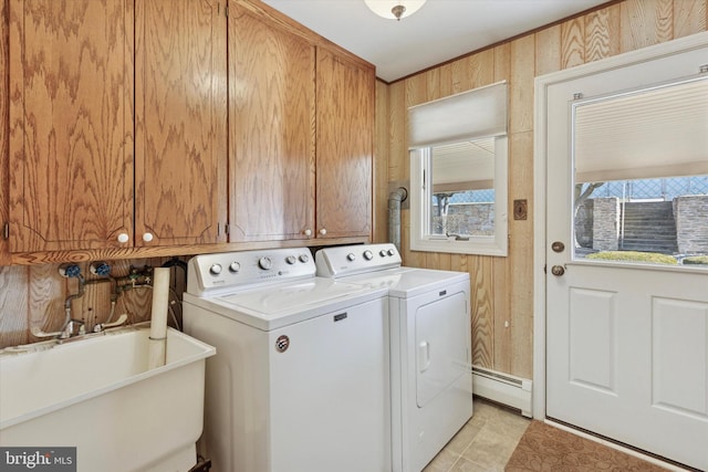 washroom with wooden walls, washer and clothes dryer, a baseboard radiator, cabinet space, and a sink