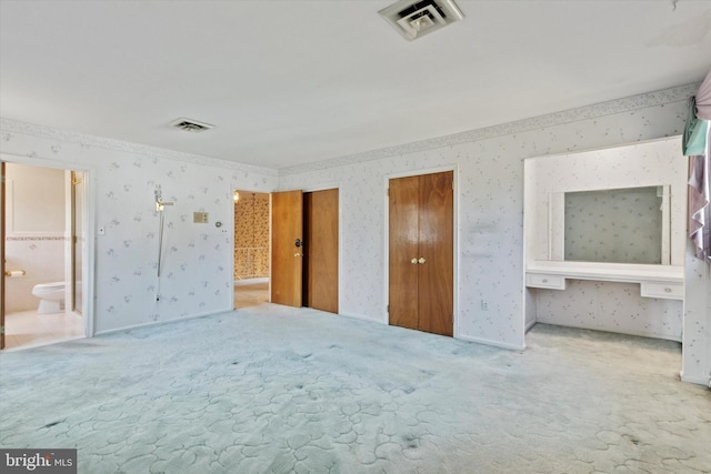 unfurnished bedroom with wallpapered walls, visible vents, multiple closets, and carpet floors