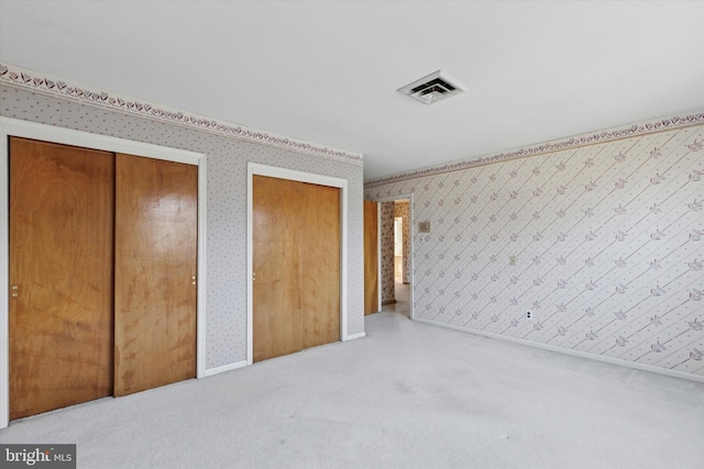 unfurnished bedroom with visible vents, two closets, carpet, wallpapered walls, and baseboards