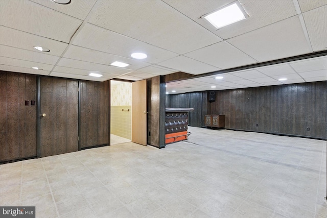 finished below grade area with tile patterned floors, a drop ceiling, and wood walls