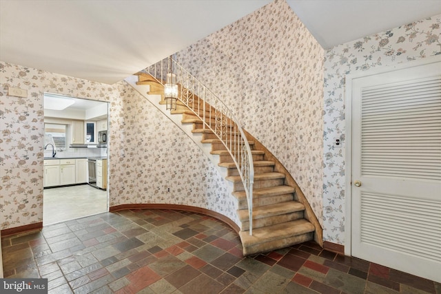 stairs with baseboards, stone tile flooring, and wallpapered walls