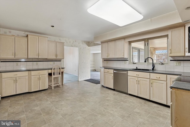 kitchen with light brown cabinets, a sink, stainless steel dishwasher, dark countertops, and wallpapered walls