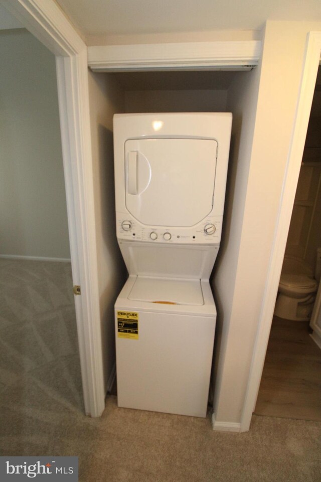 washroom featuring baseboards, carpet flooring, and stacked washer / dryer