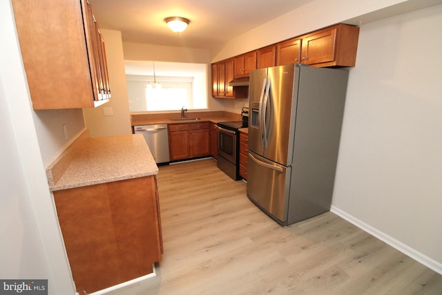 kitchen with brown cabinetry, light wood finished floors, a sink, under cabinet range hood, and appliances with stainless steel finishes