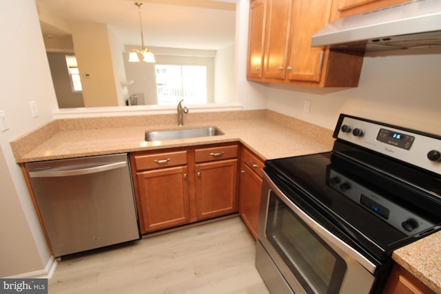 kitchen featuring under cabinet range hood, brown cabinets, light wood-style flooring, stainless steel appliances, and a sink