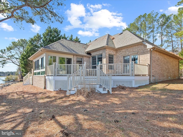 exterior space with a wooden deck, brick siding, a sunroom, and roof with shingles