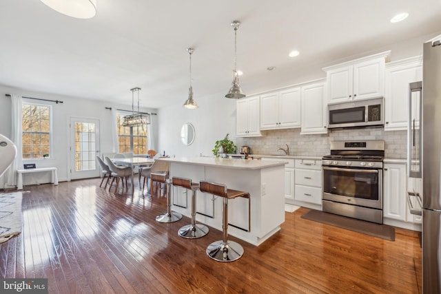 kitchen with stainless steel appliances, backsplash, dark wood-style floors, and white cabinetry