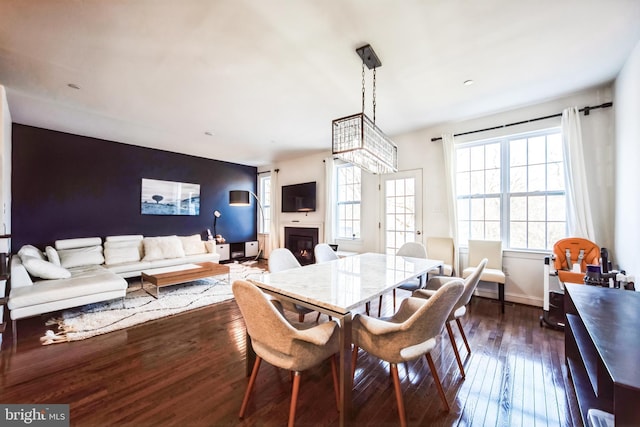 dining area with baseboards, dark wood-type flooring, a glass covered fireplace, and an accent wall