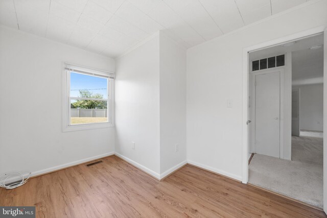 empty room with baseboards, visible vents, ornamental molding, and light wood finished floors