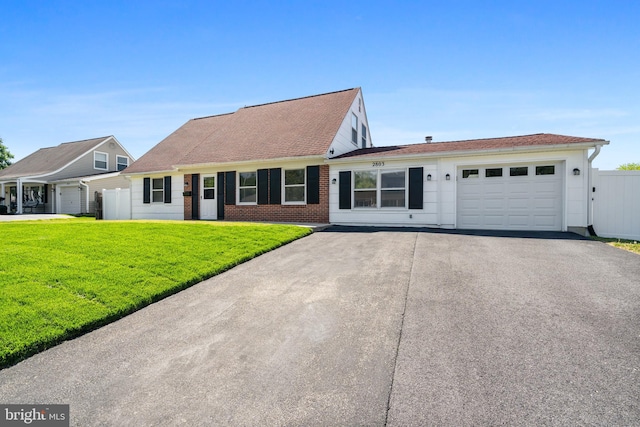 view of front of house with fence, an attached garage, a front lawn, brick siding, and driveway