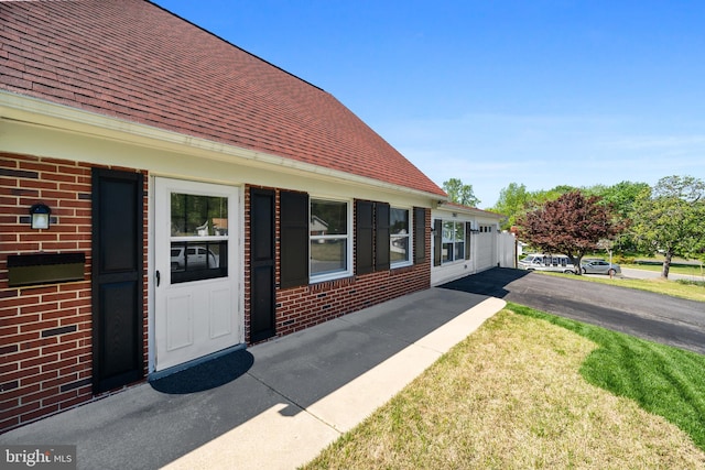 view of exterior entry featuring a shingled roof, a yard, and brick siding