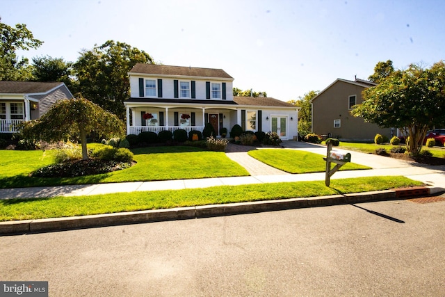 colonial-style house with french doors, driveway, covered porch, and a front yard