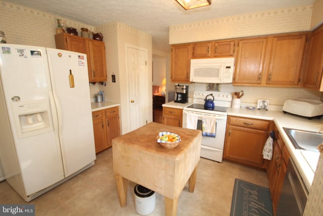 kitchen featuring a sink, wallpapered walls, white appliances, light countertops, and light floors