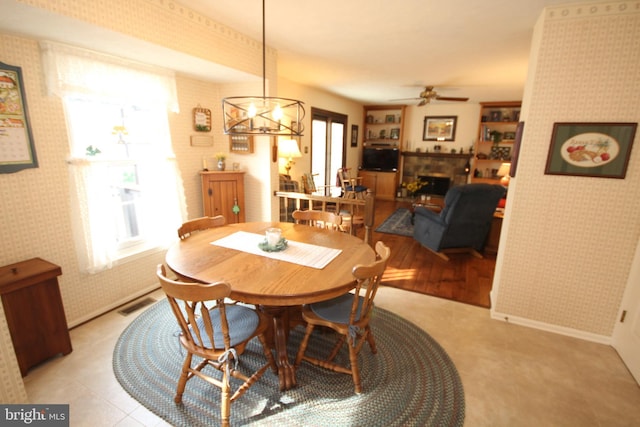 dining room with visible vents, ceiling fan with notable chandelier, a fireplace, wallpapered walls, and baseboards