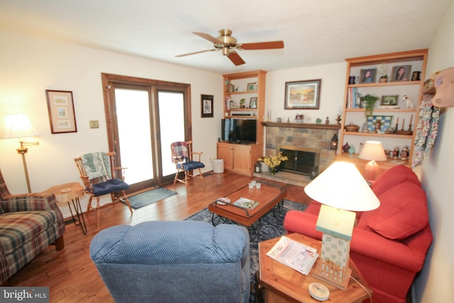 living area with a stone fireplace, wood finished floors, and a ceiling fan