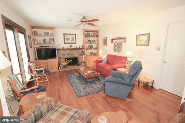 living area with a ceiling fan, wood finished floors, and a fireplace with raised hearth