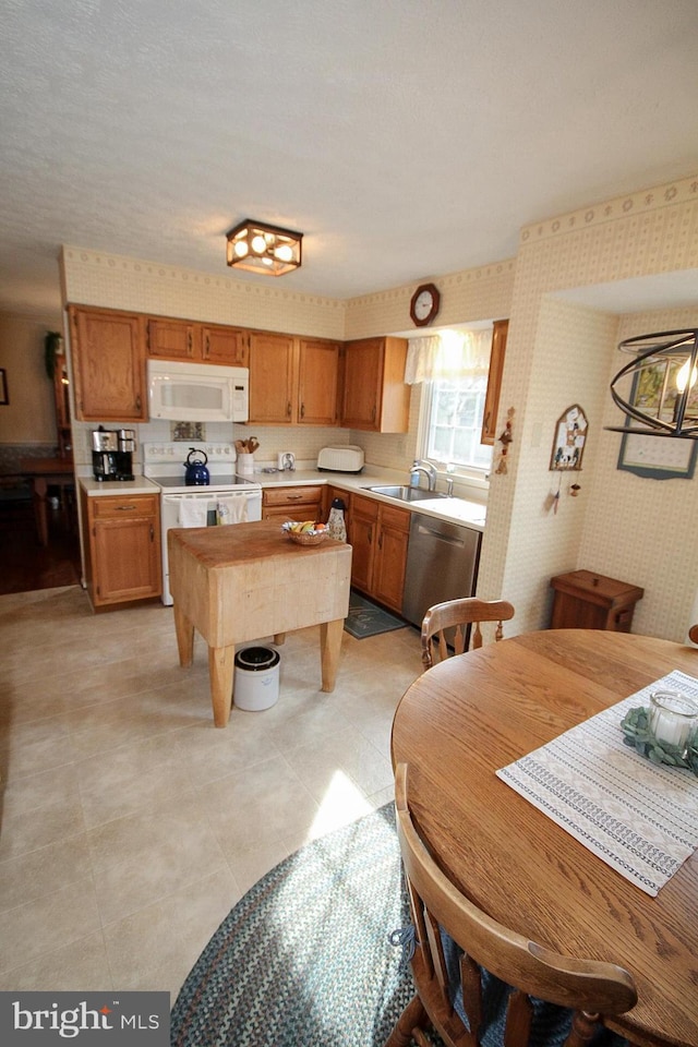 kitchen with wallpapered walls, light countertops, brown cabinetry, white appliances, and a sink