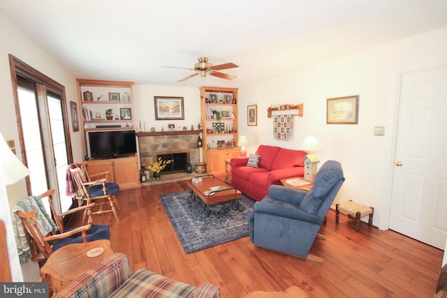 living area with a fireplace, a ceiling fan, and wood-type flooring