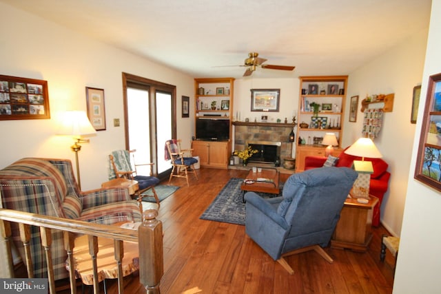 living area with a stone fireplace, a ceiling fan, and hardwood / wood-style flooring