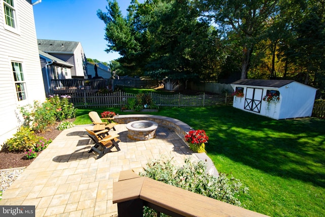 view of yard featuring fence, an outdoor fire pit, a storage shed, a patio area, and an outbuilding