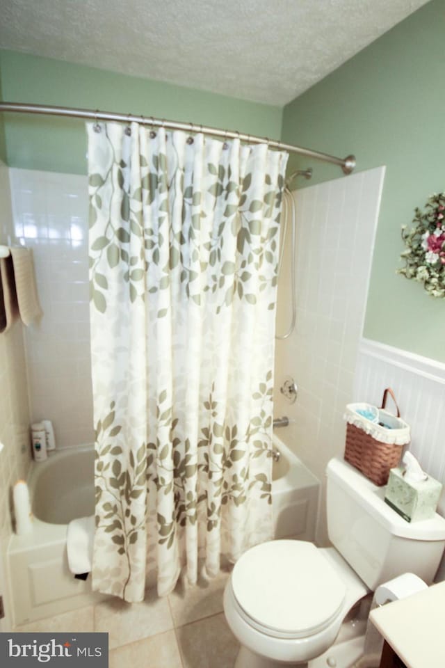 full bathroom with tile patterned flooring, shower / bath combo with shower curtain, toilet, wainscoting, and a textured ceiling