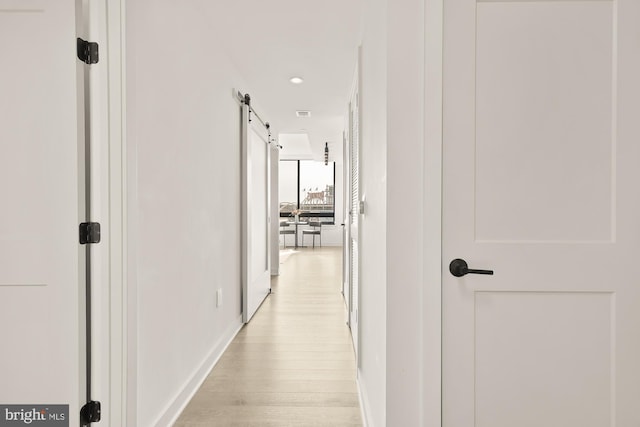 hall featuring a barn door, baseboards, and light wood finished floors