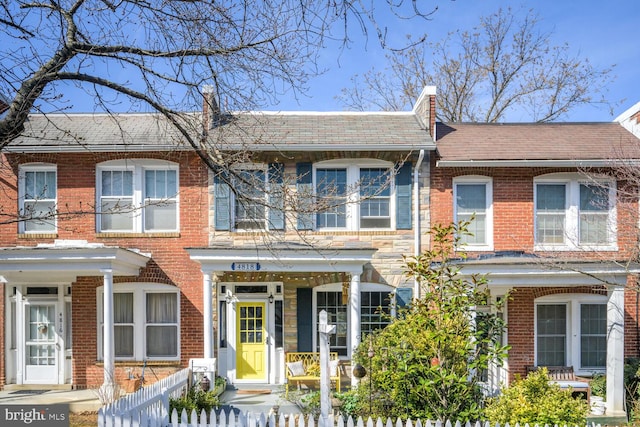 view of property with a fenced front yard, brick siding, and roof with shingles