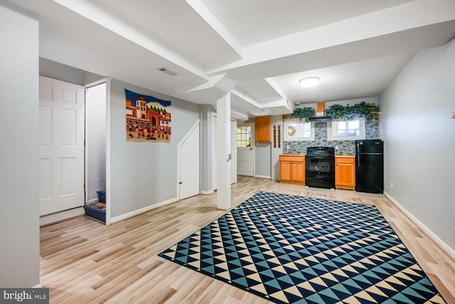 kitchen featuring black appliances, a wealth of natural light, light wood finished floors, and backsplash