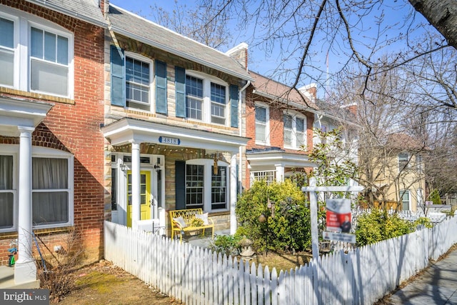 view of front of property with brick siding, a fenced front yard, and a shingled roof