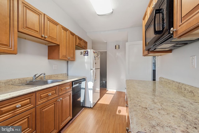 kitchen with light wood finished floors, black microwave, dishwasher, freestanding refrigerator, and a sink