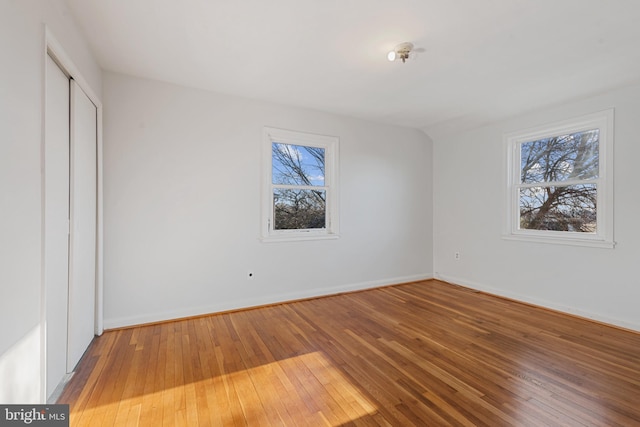 unfurnished bedroom with hardwood / wood-style flooring, baseboards, a closet, and lofted ceiling