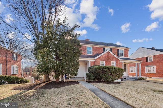 view of front facade with brick siding, a chimney, and a front yard