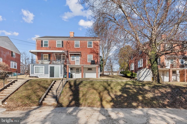 view of property featuring brick siding, a front lawn, stairs, a chimney, and a balcony