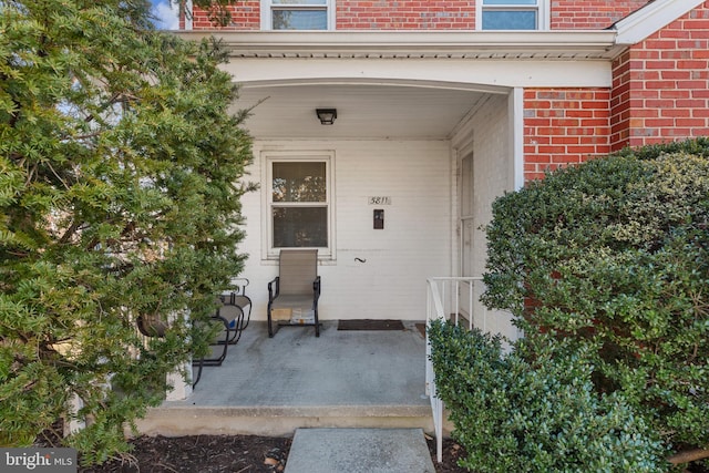 view of exterior entry with brick siding and a porch