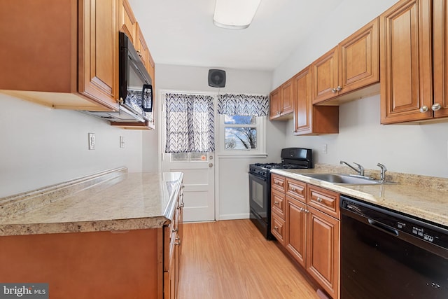 kitchen featuring light wood-type flooring, light countertops, brown cabinetry, black appliances, and a sink