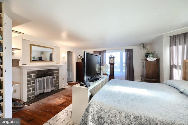 bedroom featuring wood finished floors, a fireplace, and arched walkways