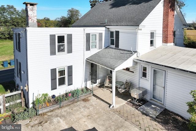 back of property with a patio, a chimney, and a shingled roof