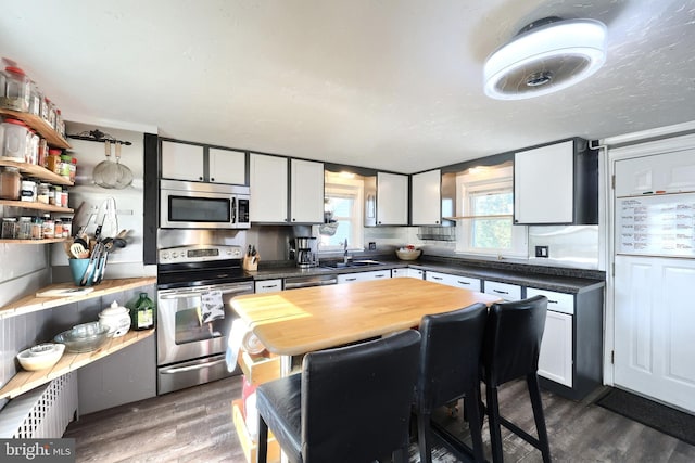 kitchen with a sink, wood counters, dark wood-style floors, white cabinetry, and appliances with stainless steel finishes