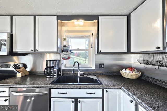 kitchen with white cabinetry, dark countertops, stainless steel appliances, and a sink