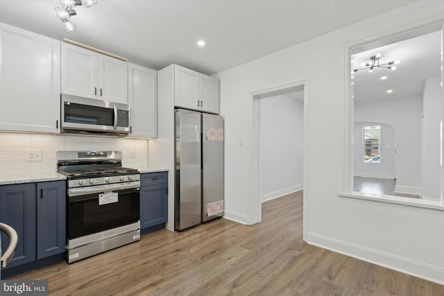 kitchen with light stone counters, backsplash, light wood-style floors, and appliances with stainless steel finishes