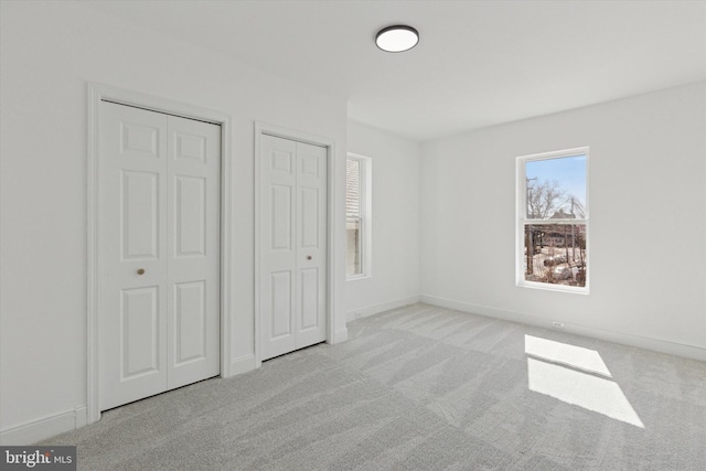 unfurnished bedroom with baseboards, two closets, and carpet floors