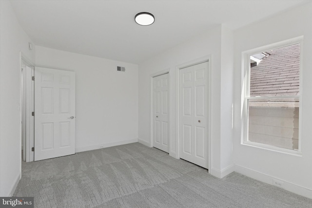 unfurnished bedroom with baseboards, carpet flooring, two closets, and visible vents