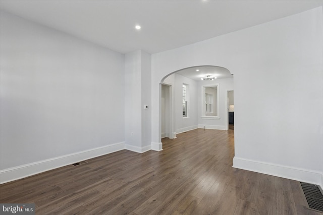 empty room with arched walkways, visible vents, dark wood-type flooring, and baseboards