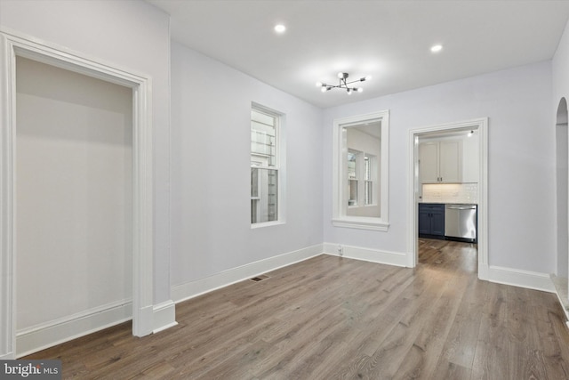 unfurnished dining area with wood finished floors, visible vents, baseboards, recessed lighting, and arched walkways